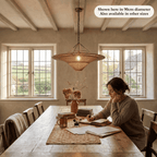 Woman writing in a notebook at a large dining table beneath the Sol wicker lampshade
